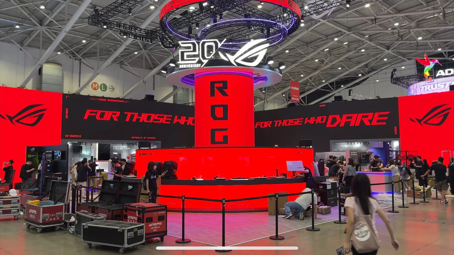 2026 南港資訊展華碩 ROG 展位，中央設有紅色圓柱螢幕與 20 週年標誌，周圍為大型紅色背板與展示區，現場工作人員正在佈展。